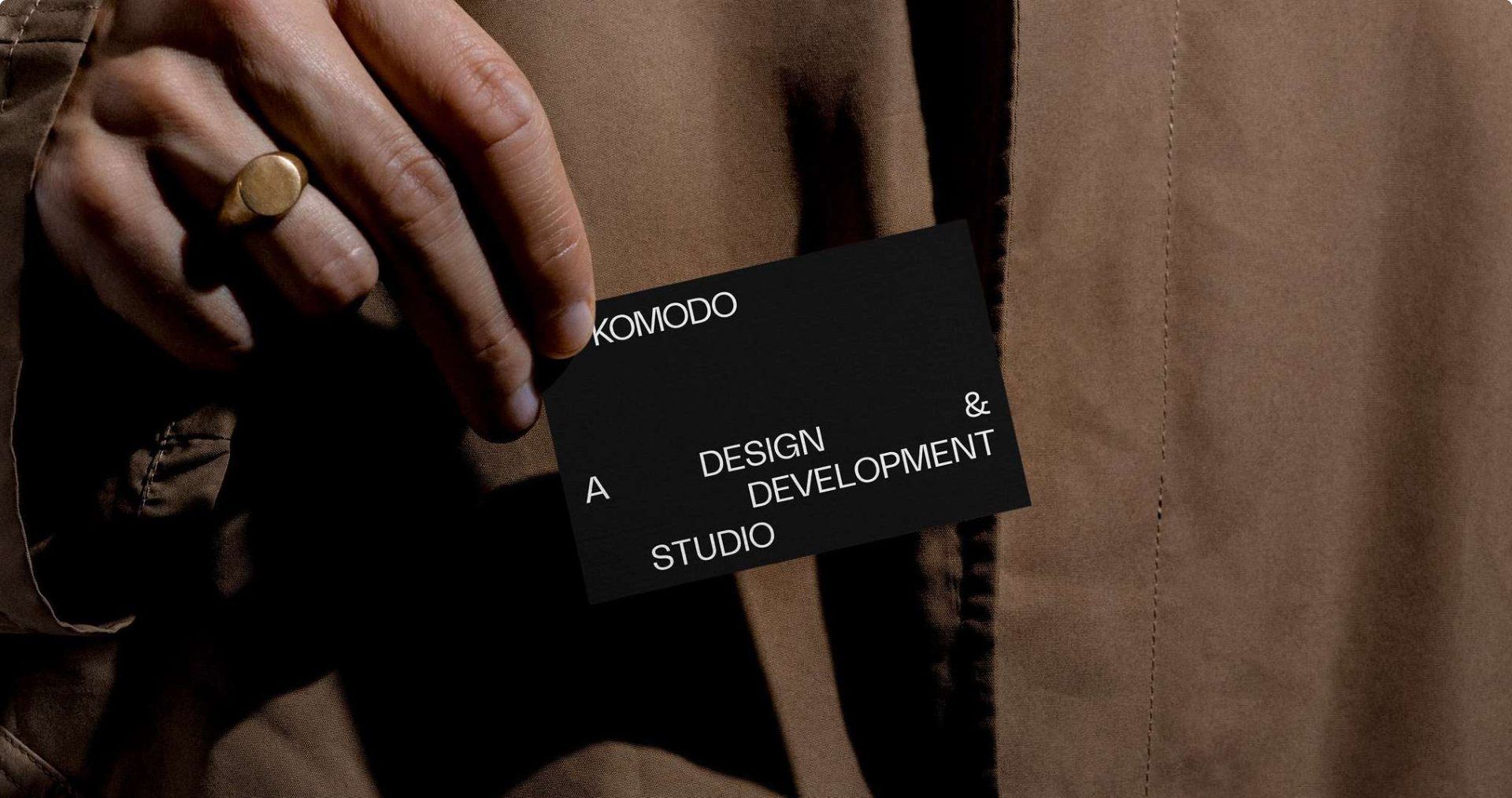 A black Komodo business card being drawn from a coat pocket, the wordmark and the studio line stepped across it.