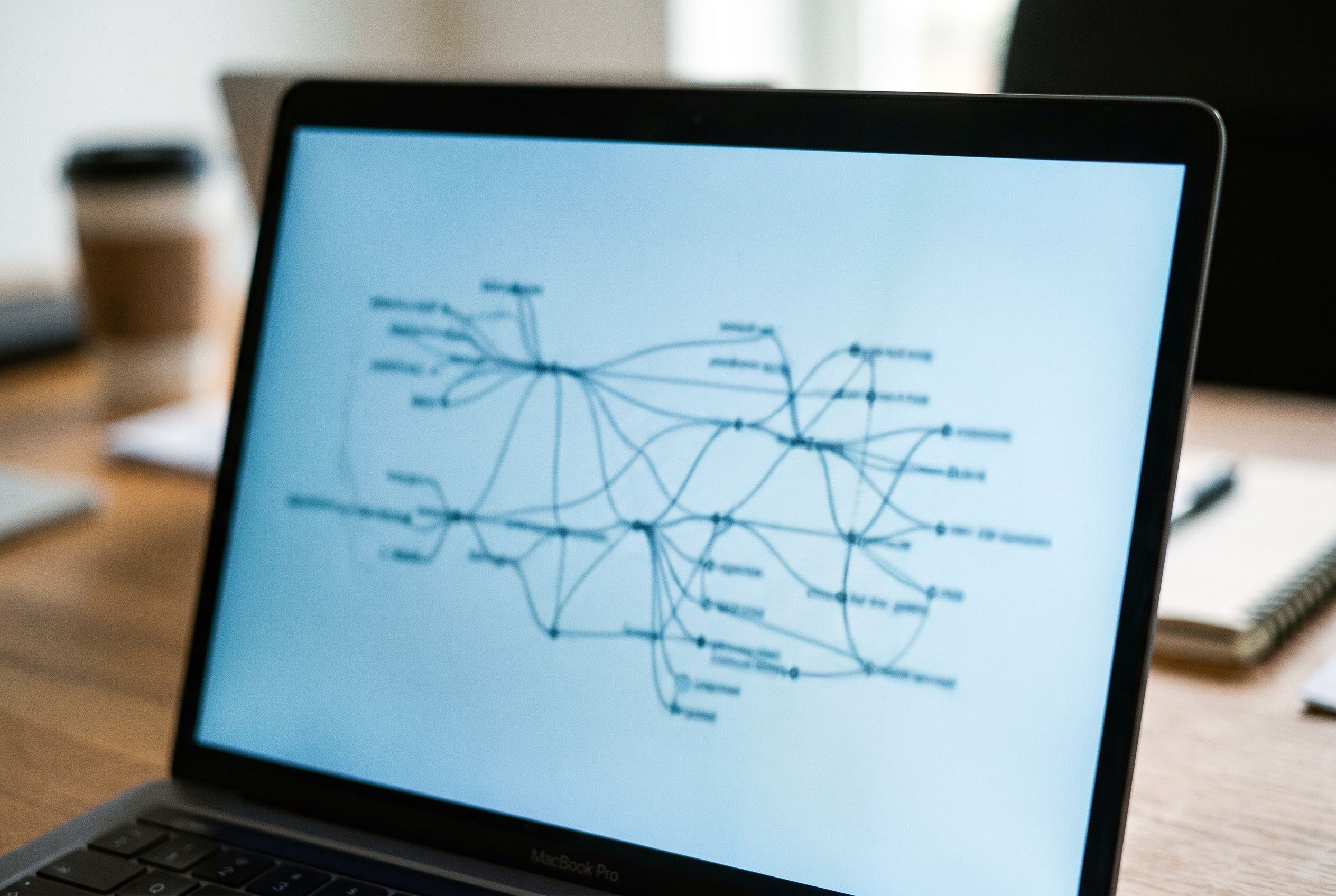 A laptop showing an abstract network of connected nodes and lines on a pale blue ground.