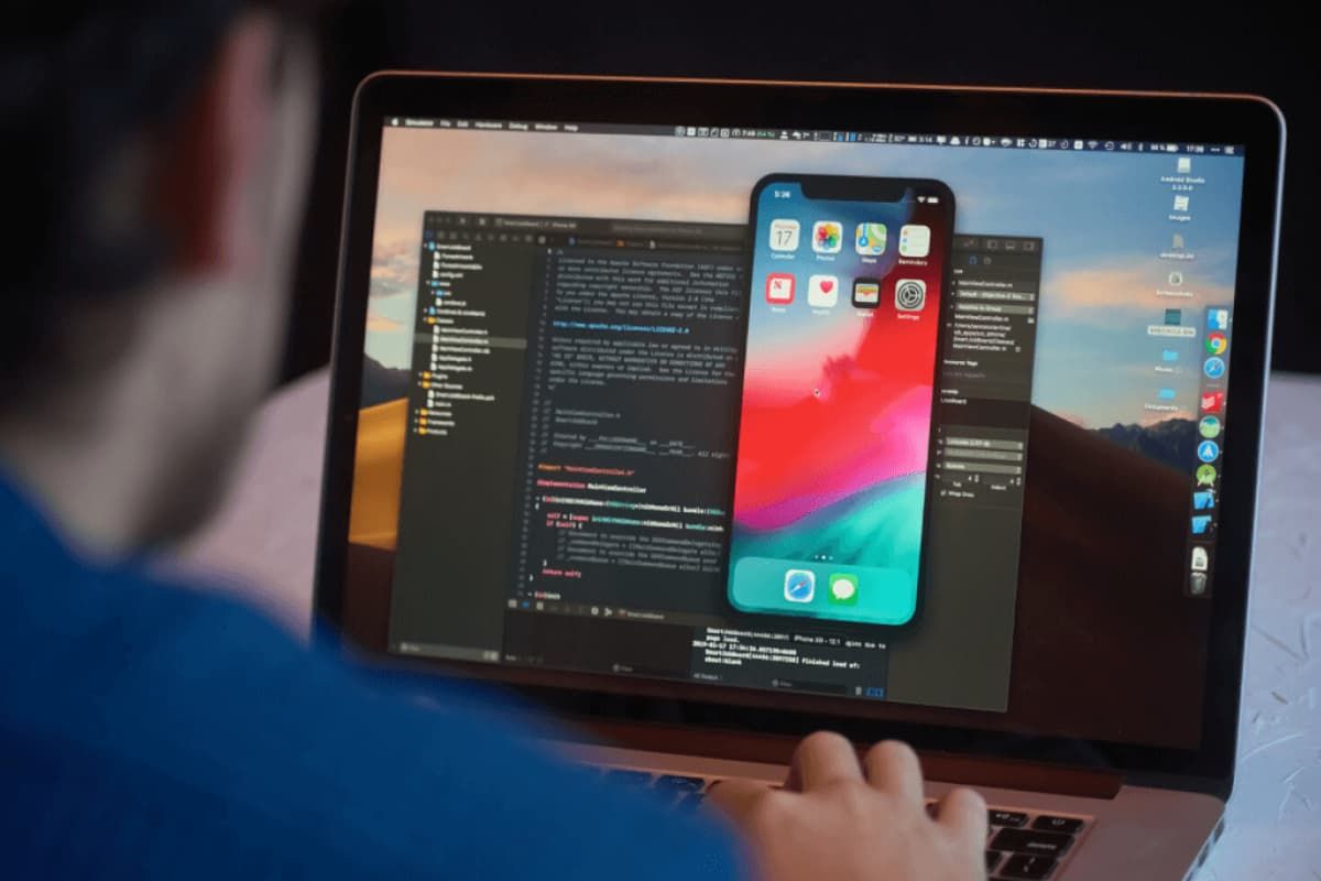 A person looking at a laptop with a mobile screen, code editor in the background