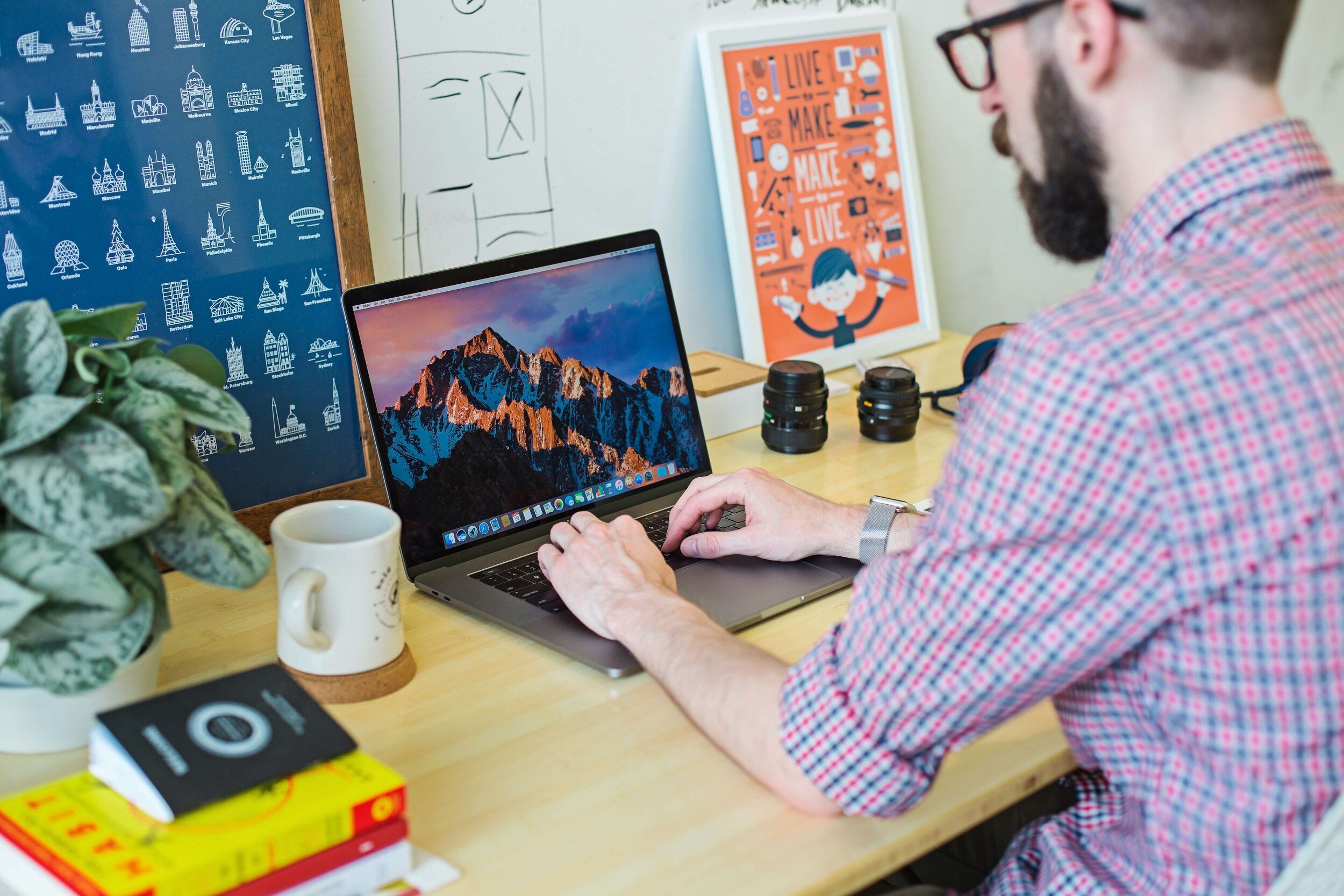 A man wearing glasses and a check shirt working on a laptop