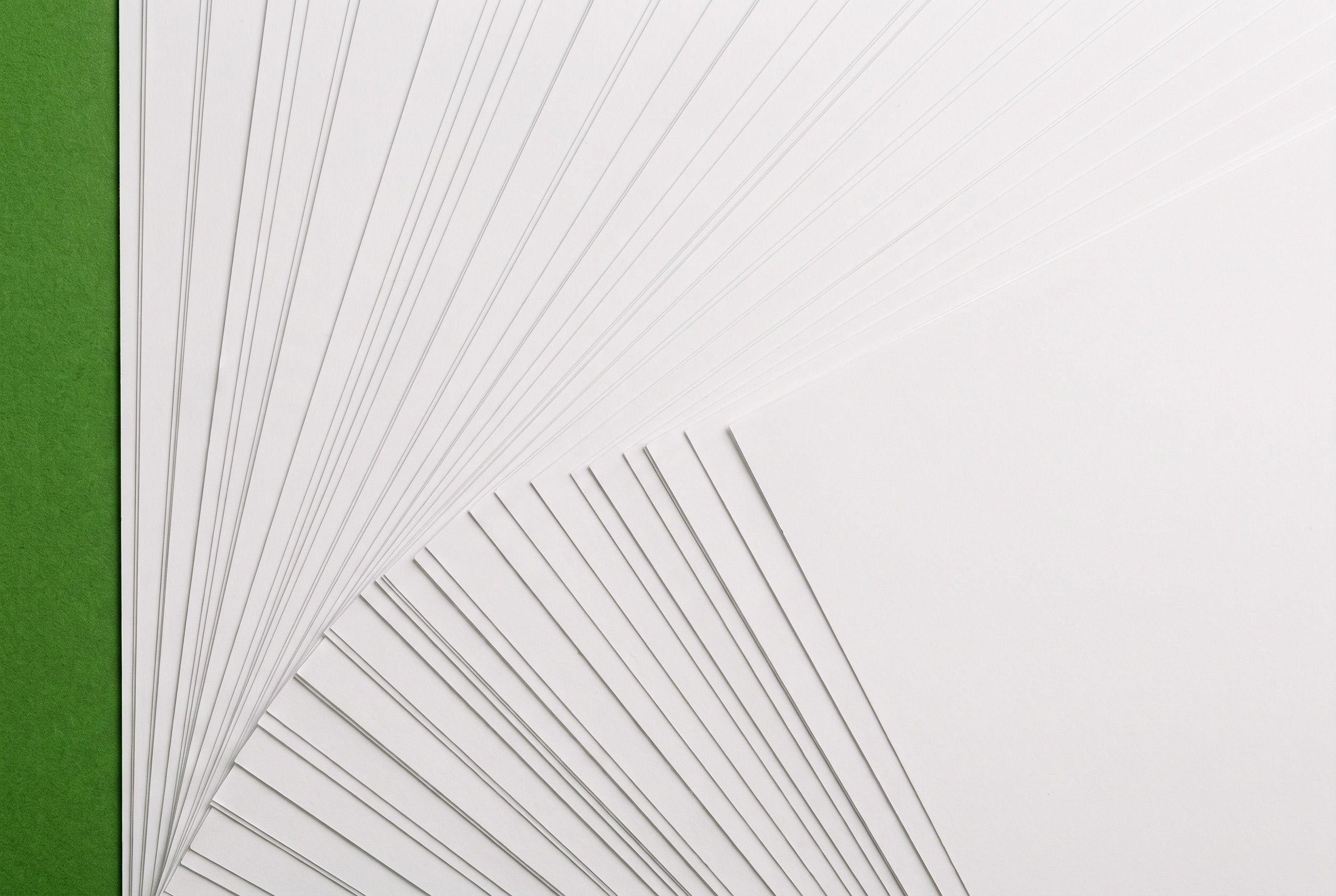 Sheets of white paper fanned in a regular overlapping stack on a green surface, seen from above.