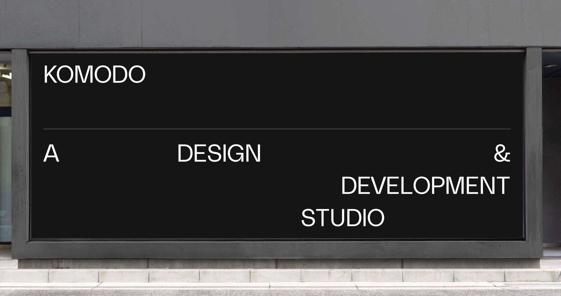 The Komodo wordmark above the words A DESIGN AND DEVELOPMENT STUDIO, arranged across a wide black signage panel so each phrase sits on a different column.